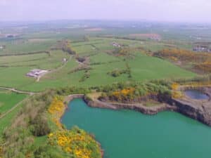 Aerial view of rural landscape with green fields, turquoise lake, rocky cliffs, under clear sky.
