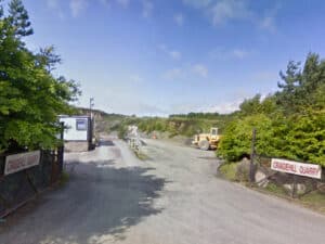Entrance to Craigehill Quarry with gates, signs, trees, a portable building, and construction machinery.