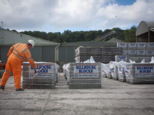 Person in safety gear examines Hillhouse Blocks at industrial site with sheds and conveyor.