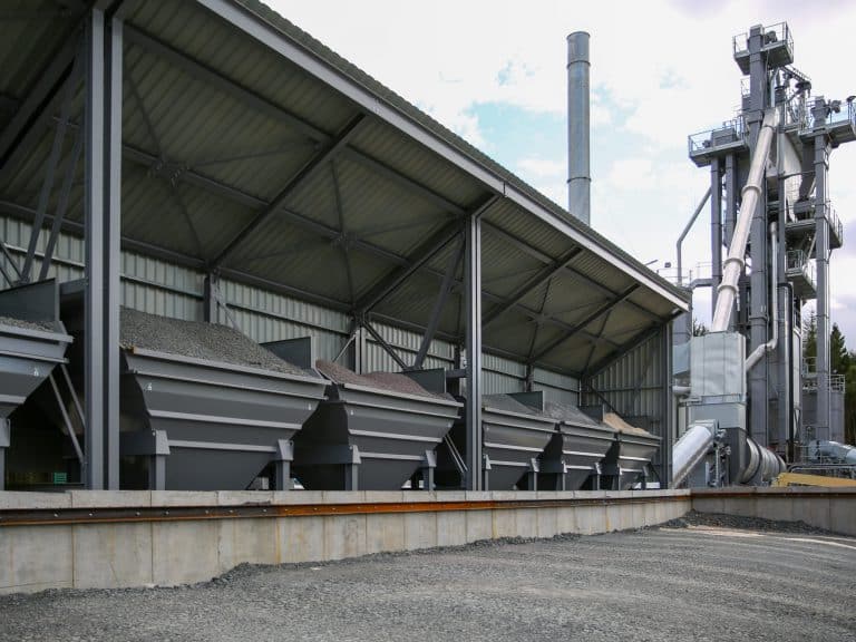 Industrial facility with metal storage bins for gravel, sloped roof, chimney, and machinery.