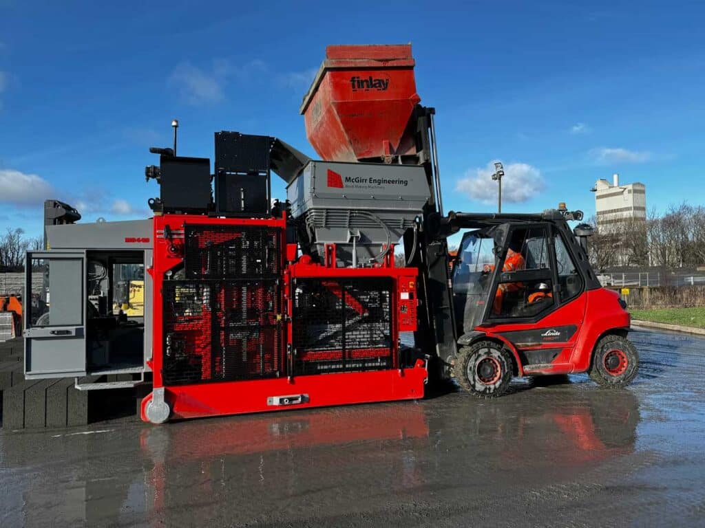 Forklift transporting industrial machinery on wet surface with clear sky background.
