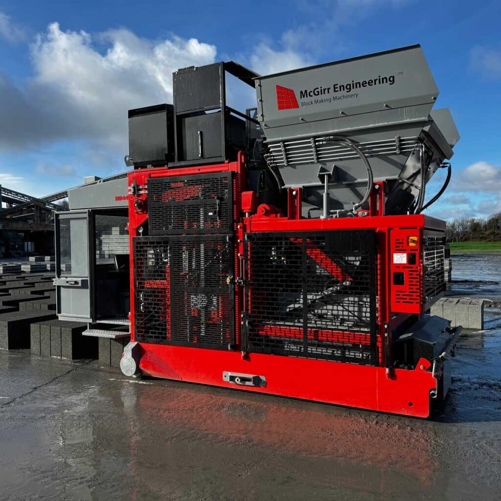 Industrial block-making machinery by McGirr Engineering, grey and red, on concrete with blocks nearby.
