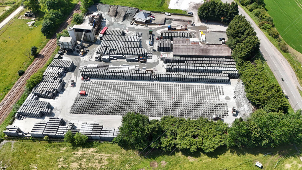 Aerial view of industrial site with stacked concrete blocks, machinery, buildings, road, and railway.