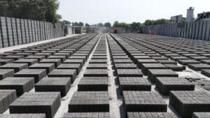 Outdoor storage yard with rows of stacked concrete blocks and industrial buildings in background