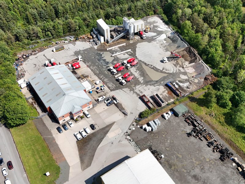 Aerial view of an industrial concrete mixing site with buildings, trucks, and storage areas.
