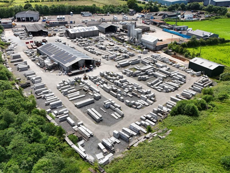 Aerial view of industrial facility with buildings, storage area, materials, vehicles, and greenery.