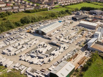 Aerial view of industrial facility with storage areas, warehouses, machinery, greenery, houses.