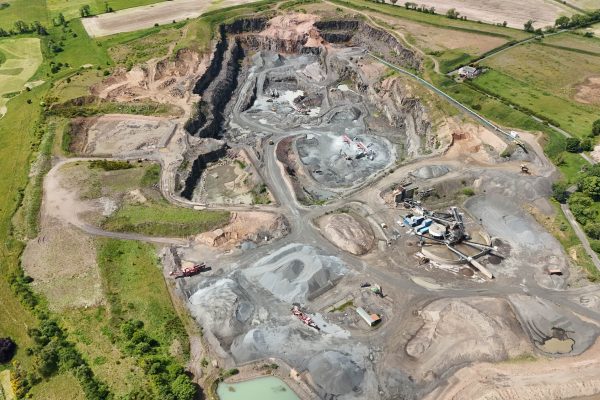 Aerial view of an open-pit quarry with excavation zones, machinery, and surrounding fields.