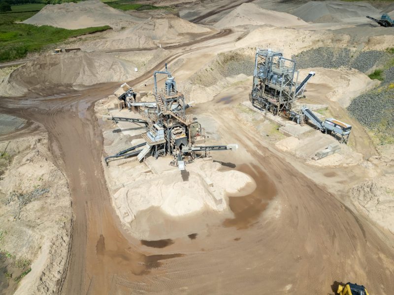 Aerial view of a sand quarry with machinery, pathways, and piles of sand in a rural setting.