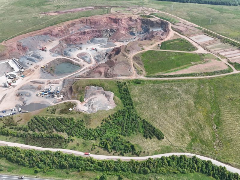 Aerial view of an open-pit quarry with excavation sites, machinery, and surrounding green fields.
