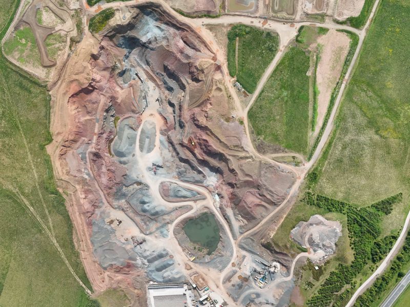 Aerial view of quarry with excavated earth, machinery, ponds, storage areas, and access roads.
