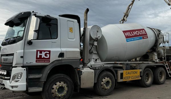 Cement mixer truck with Hillhouse Group logo and caution sign on concrete surface under cloudy sky.