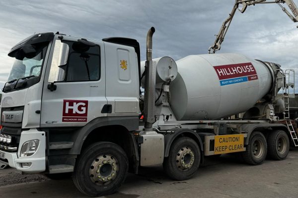 Cement mixer truck with Hillhouse Group logo and caution sign on concrete surface under cloudy sky.