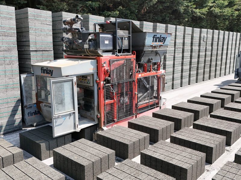 Concrete block manufacturing site with Finlay machines stacking blocks in rows and tall stacks.