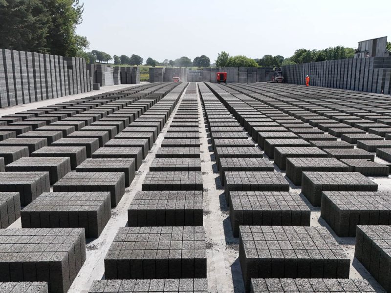 Outdoor storage yard with rows of stacked concrete blocks and industrial buildings in background