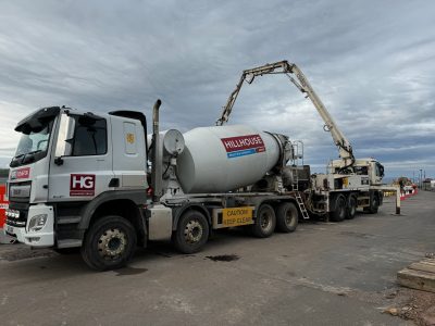 Concrete mixer truck on industrial site, Hillhouse Group, construction cones, overcast sky.
