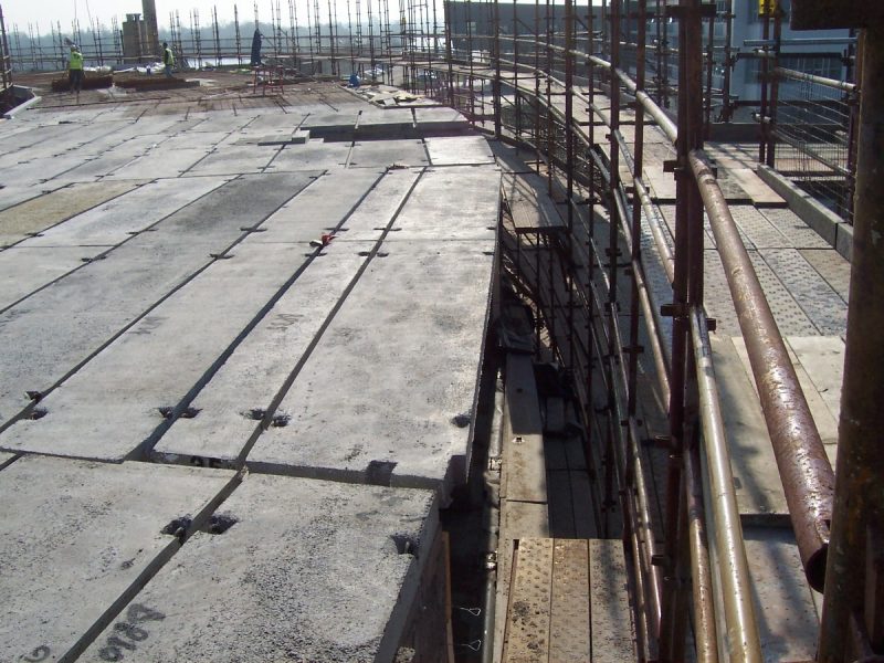 Construction site with unfinished concrete floor, scaffolding, and workers in the background.