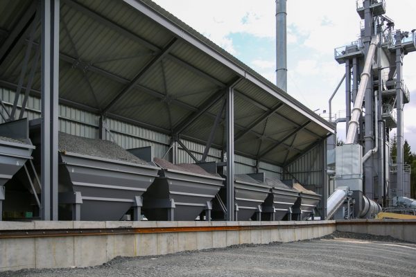 Industrial facility with metal storage bins for gravel, sloped roof, chimney, and machinery.