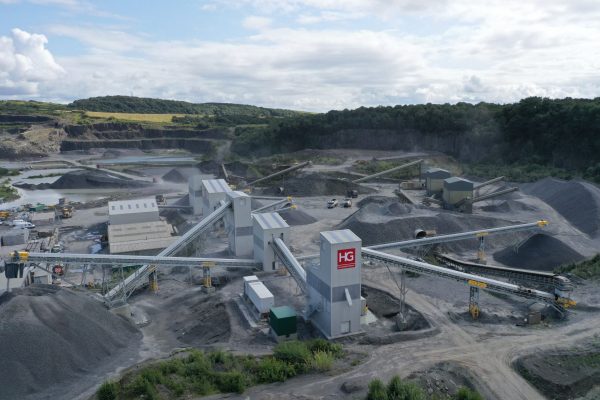 Quarry Site with Conveyors and Gravel Piles Industrial quarry with conveyors, storage, gravel piles, trees, water pits, and cloudy sky.