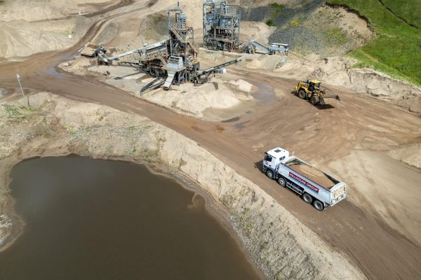 Industrial sand and gravel extraction site with machinery, vehicles, and sand piles near water.