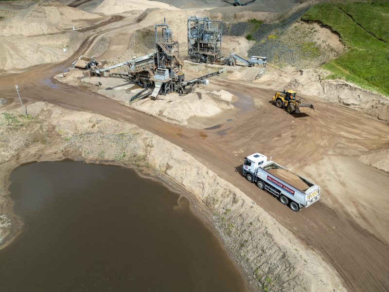 Industrial sand and gravel extraction site with machinery, vehicles, and sand piles near water.