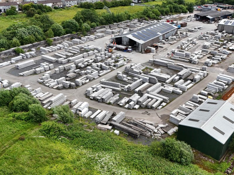 Aerial view of an industrial site with concrete slabs, warehouses, greenery, and nearby homes.