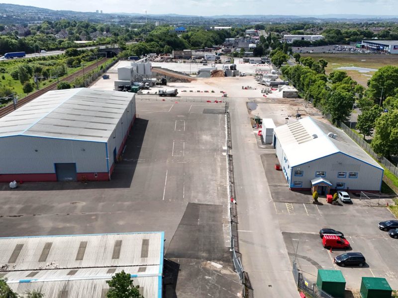 Industrial area with warehouses, parking, railway tracks, roads, trees, and surrounding buildings.