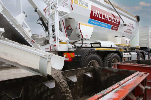 Lorry pouring concrete from chute into a container at a construction site.