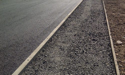 Newly constructed road with workers, gravel path, vehicles, industrial facilities, and hills.