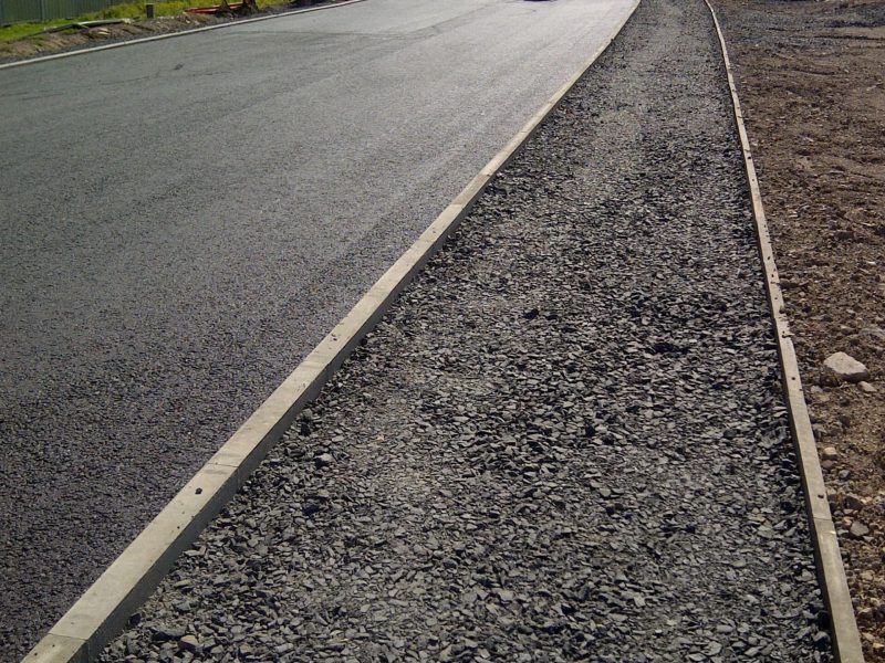 Newly constructed road with workers, gravel path, vehicles, industrial facilities, and hills.
