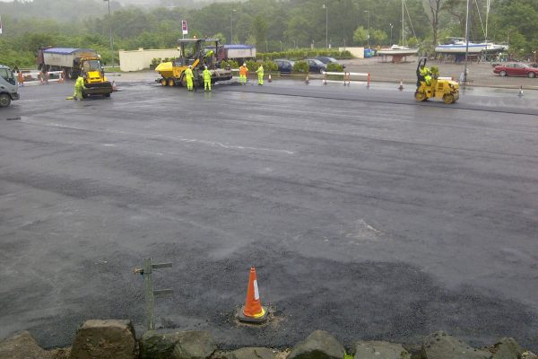 Roadworks and Construction Activity Roadworks scene with vehicles, workers in high-visibility clothing paving a large area, traffic cones.