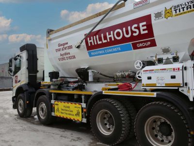 Volumetric mixer truck with construction branding and safety signs, on concrete surface.
